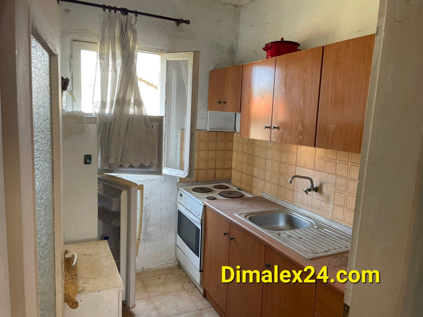 Kitchen area in a house for sale in Greece, featuring wooden cabinets, stove, sink, and window.