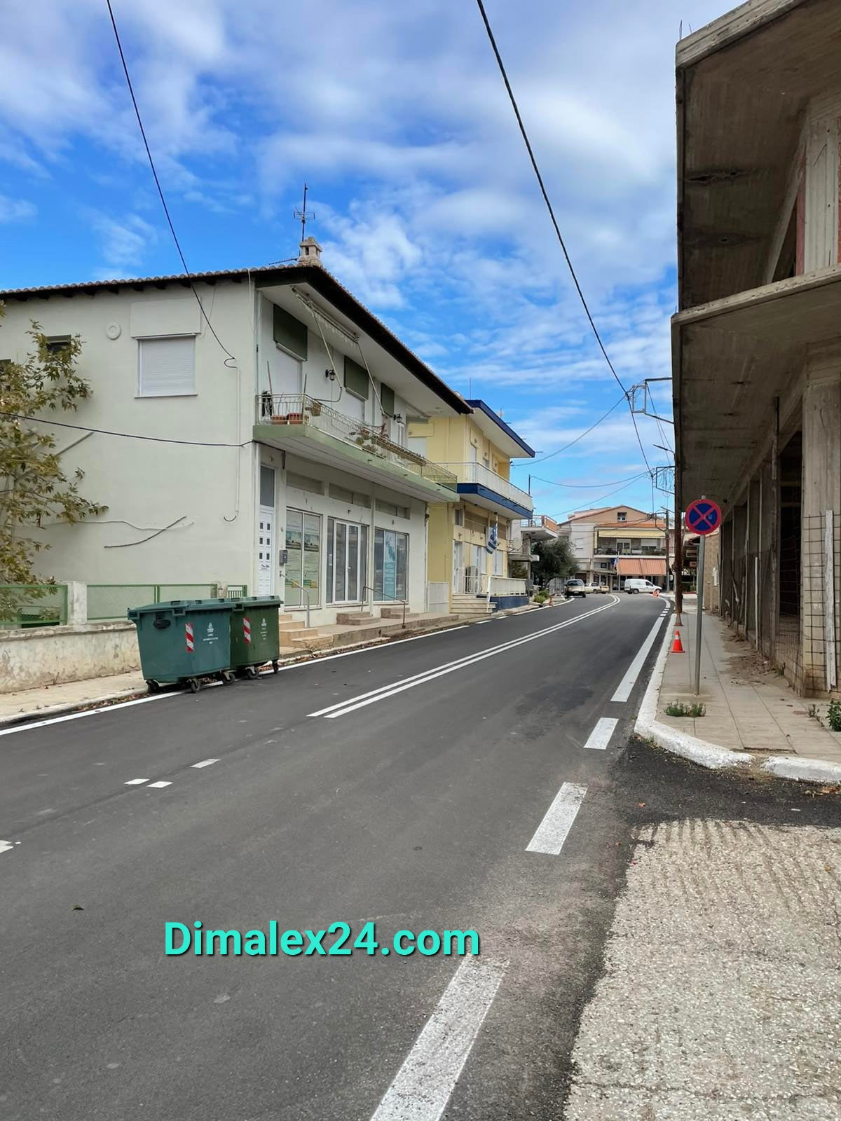 Street view in Ksilagani, North Greece, showcasing buildings and garbage bins on a clear day.