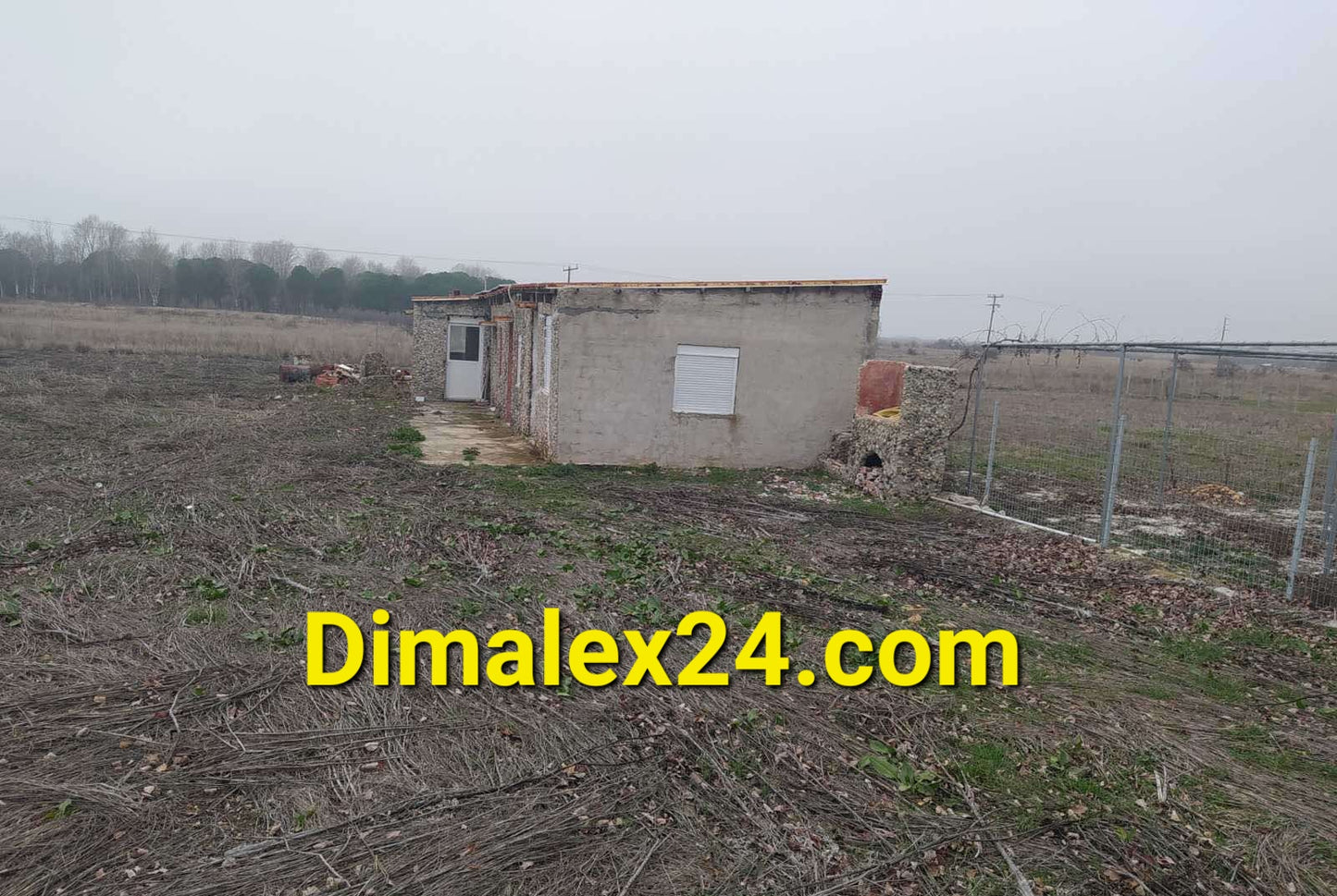 Small building on a vacant lot in northern Greece, surrounded by open fields and minimal vegetation.