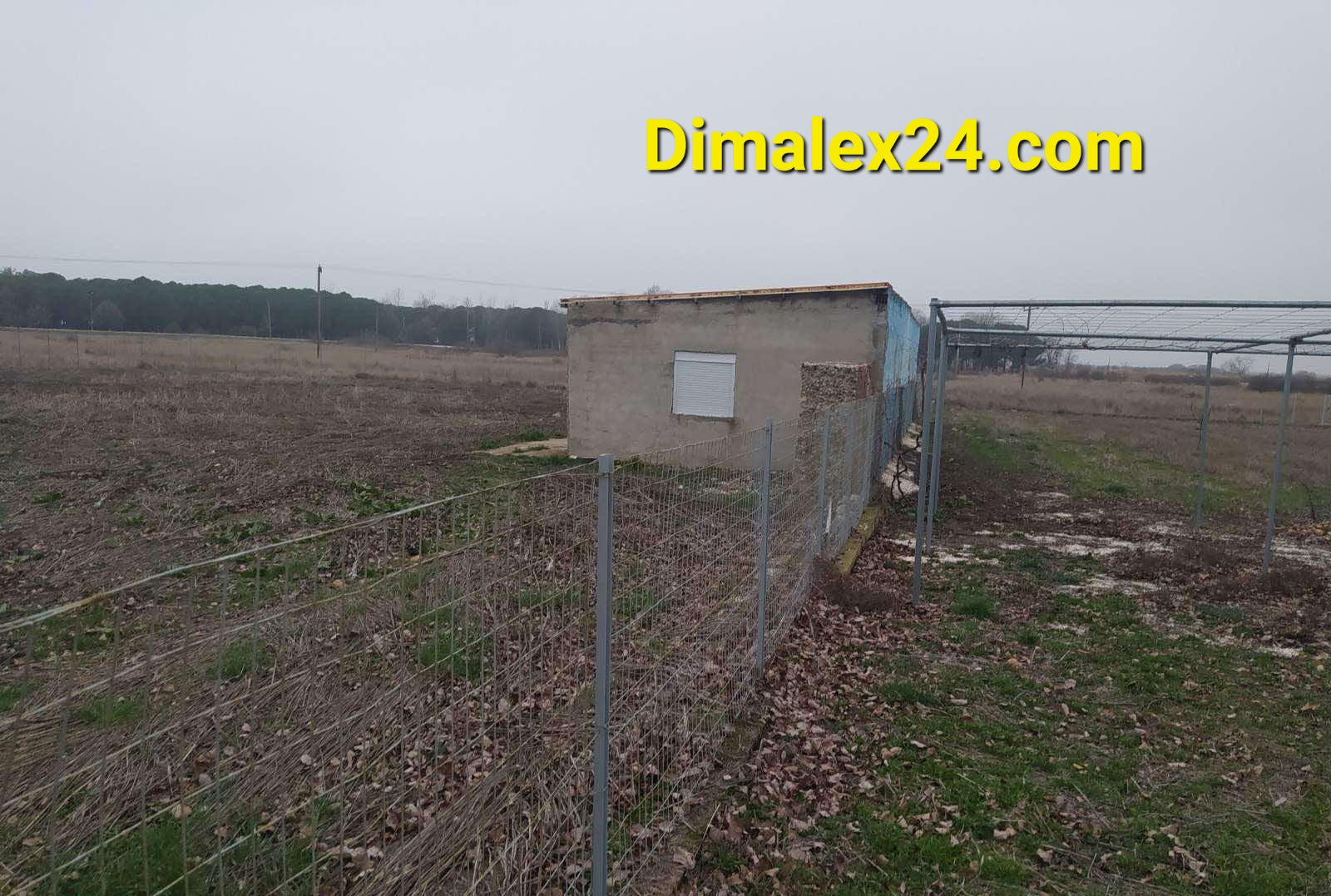 Small storage building surrounded by fencing on open land with sparse vegetation.