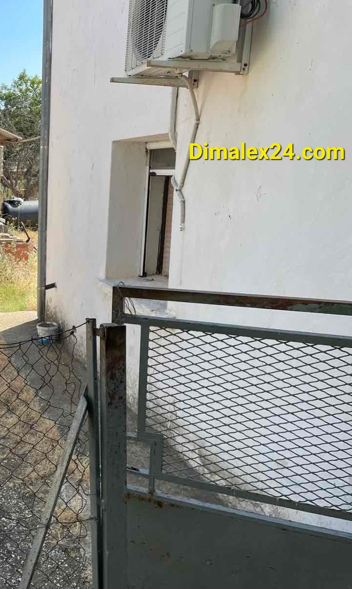 Exterior detail of a two-story house in Prosknitēs, featuring a gate and air conditioning unit.