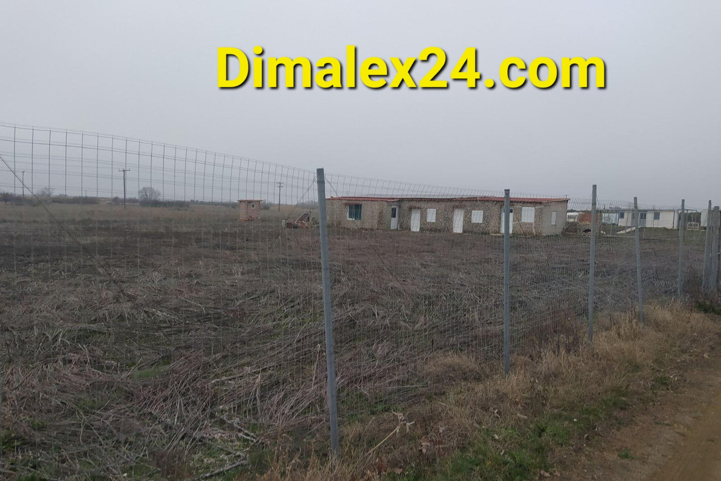 View of a fenced plot of land with an unfinished house in a rural area, showcasing potential for affordable property investment.