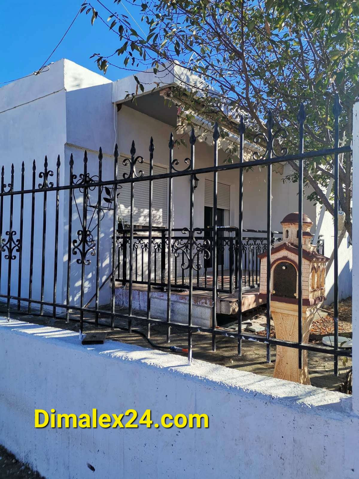 Exterior view of a house in Makri, Evros, Greece with a gated fence and tree, showcasing its peaceful surroundings.