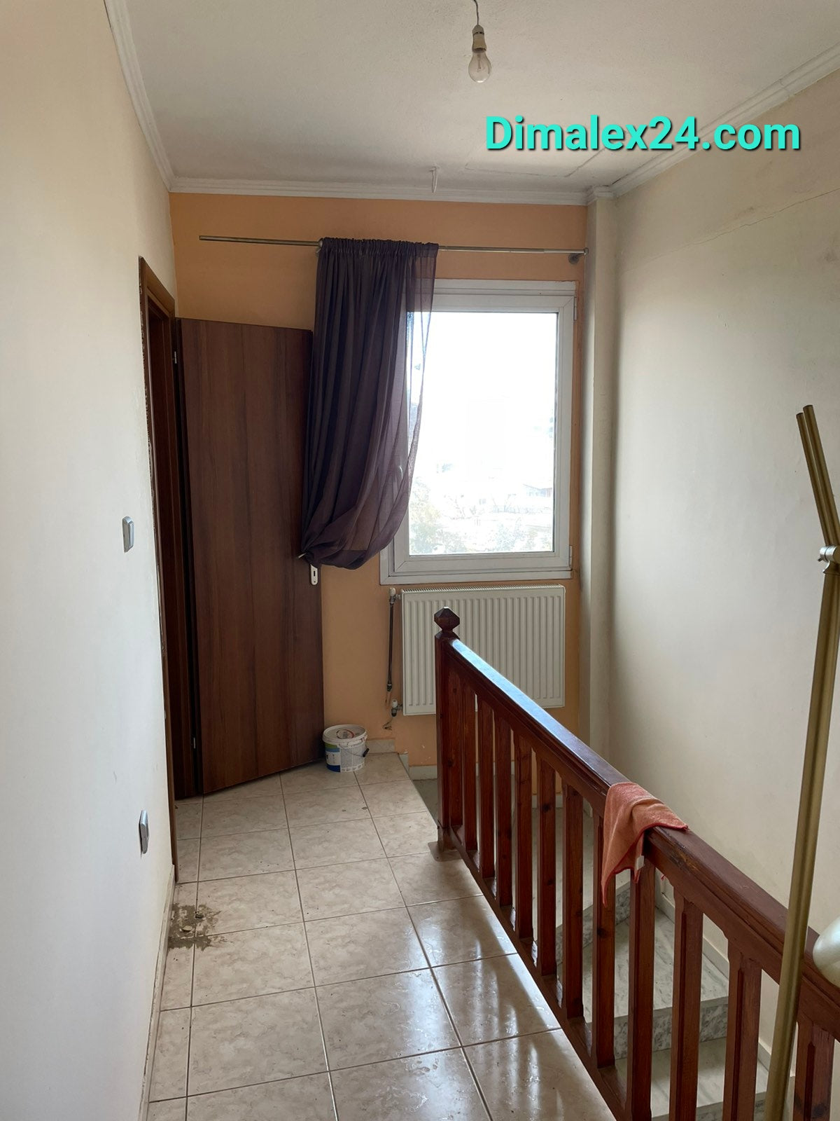 Hallway in a two-story apartment in Ksilaghani, Northern Greece, featuring a window and wooden stair railing.