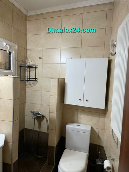 Modern bathroom with beige tiles, shower, toilet, and storage cabinet.