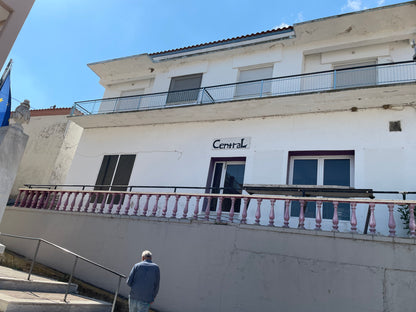 Facade of a two-story multifunctional building in Ksilagani, Greece, featuring a balcony and entrance.