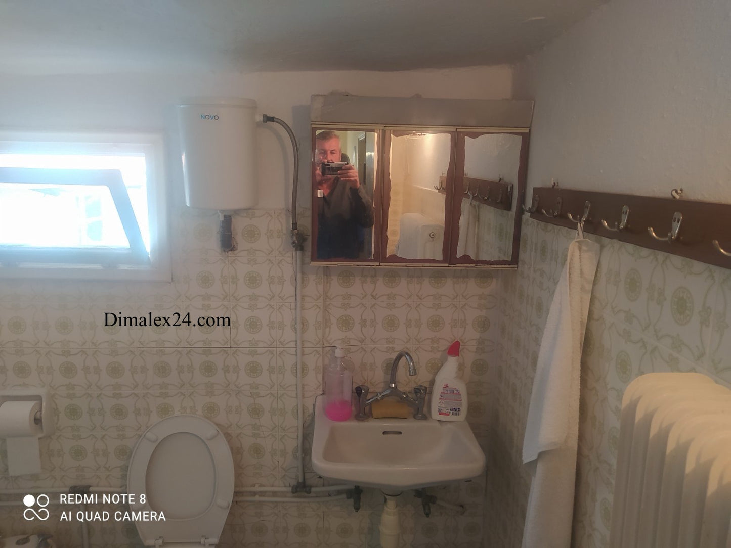 Interior view of a bathroom featuring a sink, toilet, mirror, and heating unit in a traditional style.