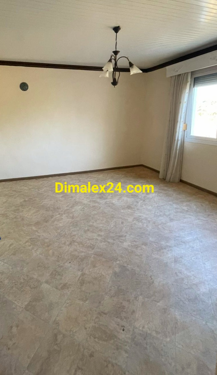 Просторна празна стая с бели стени и тавани, със светла подова настилка и голям прозорез с алуминиева дограма и ролетни щори. Имот в Северна Гърция, област родопи, Проскинитес.