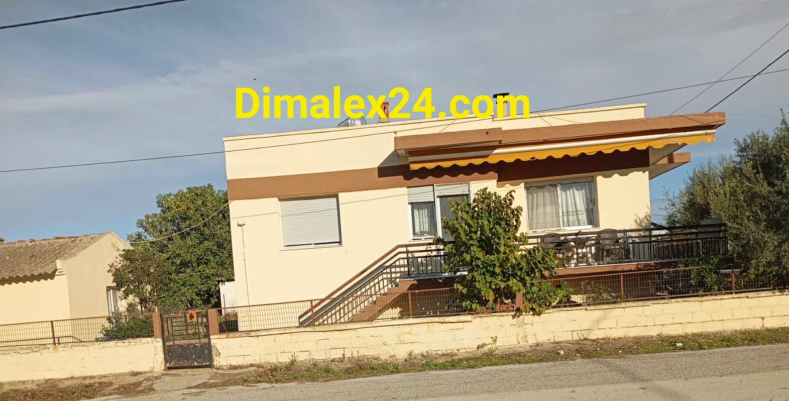 Предна фасада на къща с част от преден двор и ниска ограда с порта - имот в Гърция, село Адриани.