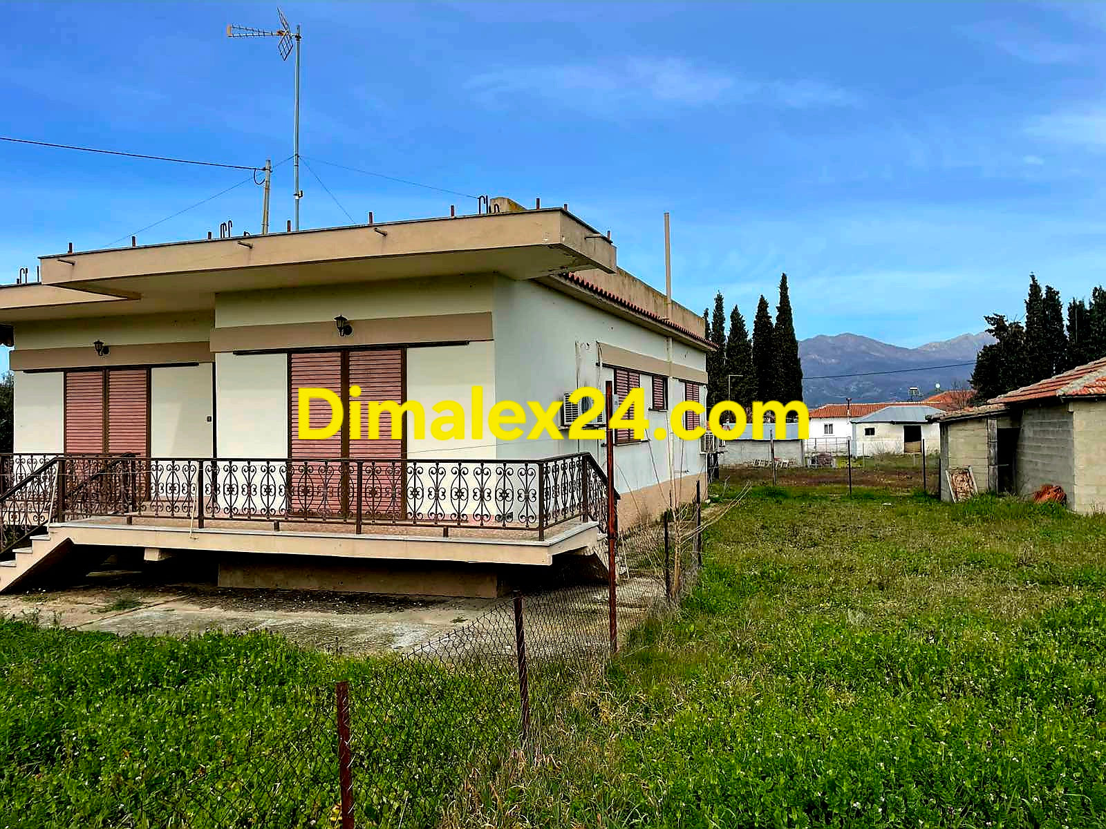 Къща в Гърция с ограден двор и асфалтов път.