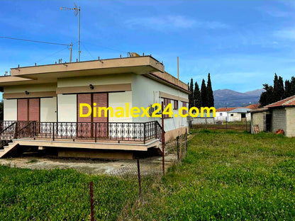 Къща в Гърция с ограден двор и асфалтов път.