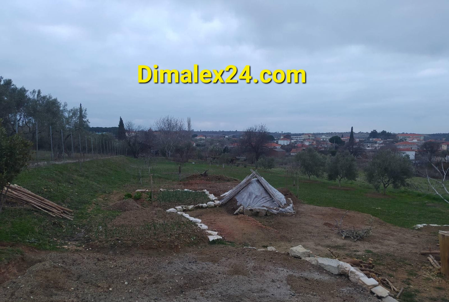 View of a rural landscape with a makeshift shelter in the foreground and a distant town under cloudy skies.