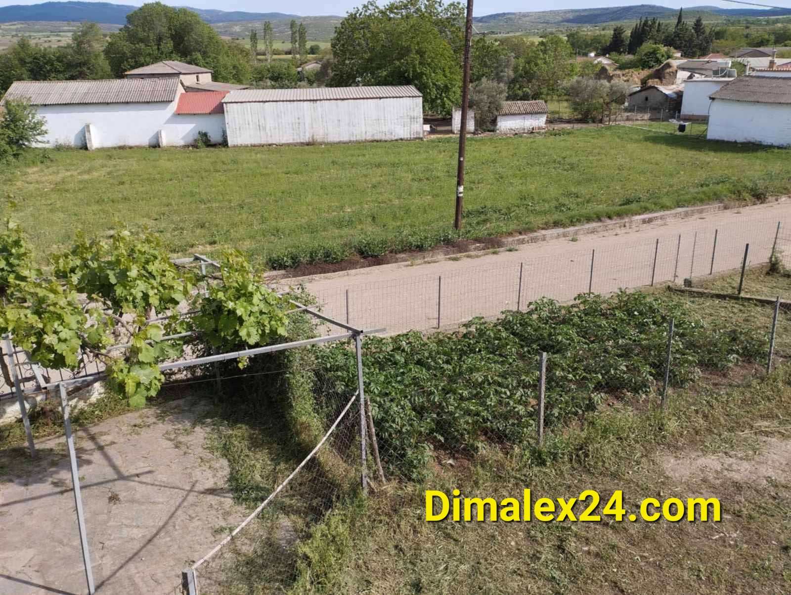 Panoramic view of a rural landscape in Greece with green fields and agricultural structures.