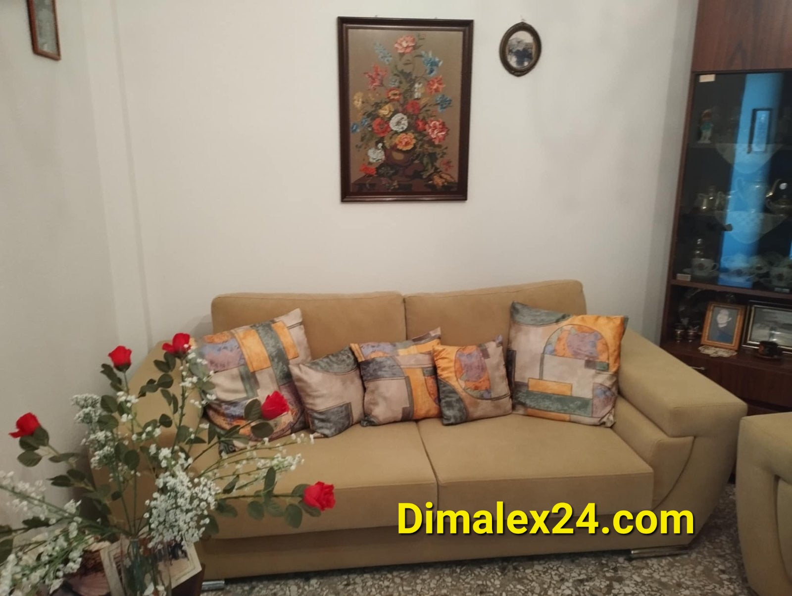 Cozy living room featuring a beige sofa with colorful cushions, floral wall art, and decorative plants.