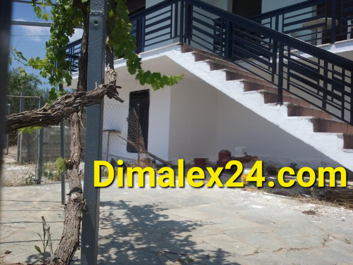 Exterior view of a house in Greece with a staircase and vine plants, ideal for peaceful living.