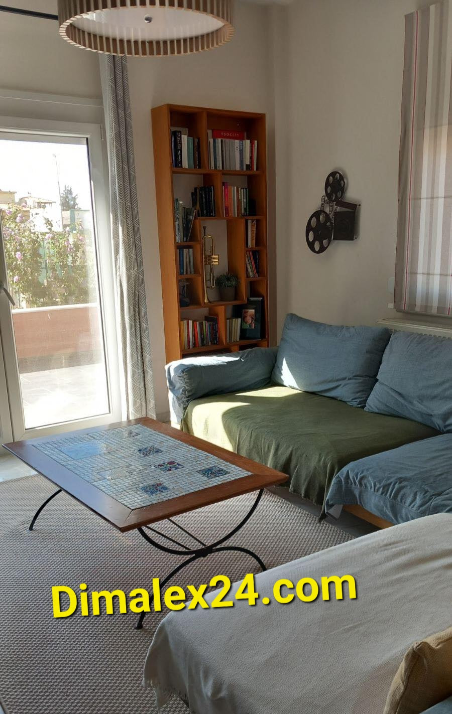 Cozy living room with a green and blue couch, wooden coffee table, bookshelf, and bright window.