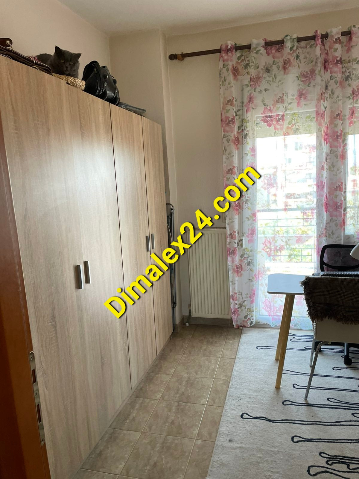 Interior view of a cozy room featuring a wooden wardrobe, floral curtains, and a desk with a chair.