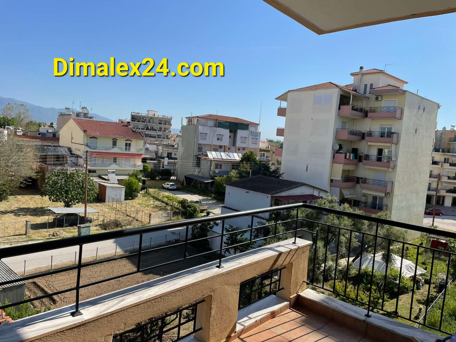 View from the balcony of a 3rd-floor apartment in Chrysoúpolis, Greece, showcasing surrounding buildings and greenery.