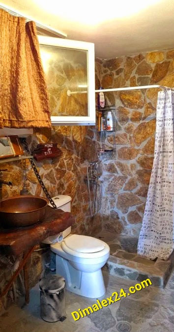 Интериор на баня с каменни стени и тоалетна, оборудвана с душ и завеса.