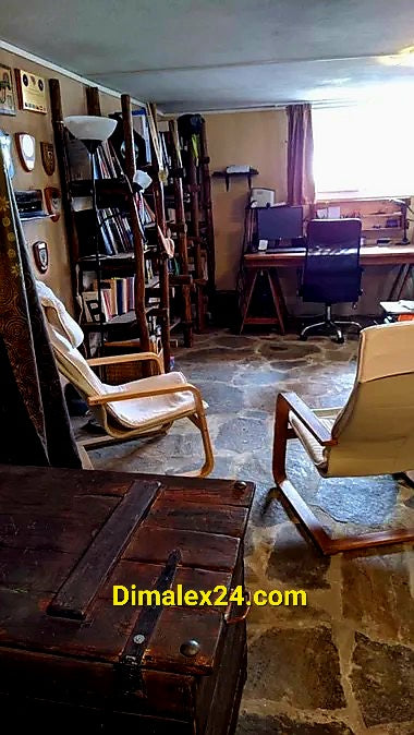 Интериор на уютен офис с каменен под, рафтове с книги и две комфортни стола.