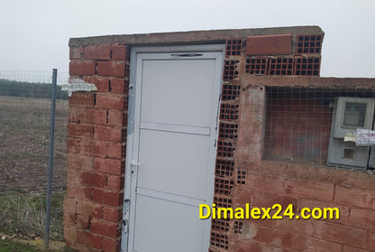White door of a brick building in an open field, featuring a simple design and surrounding fencing.