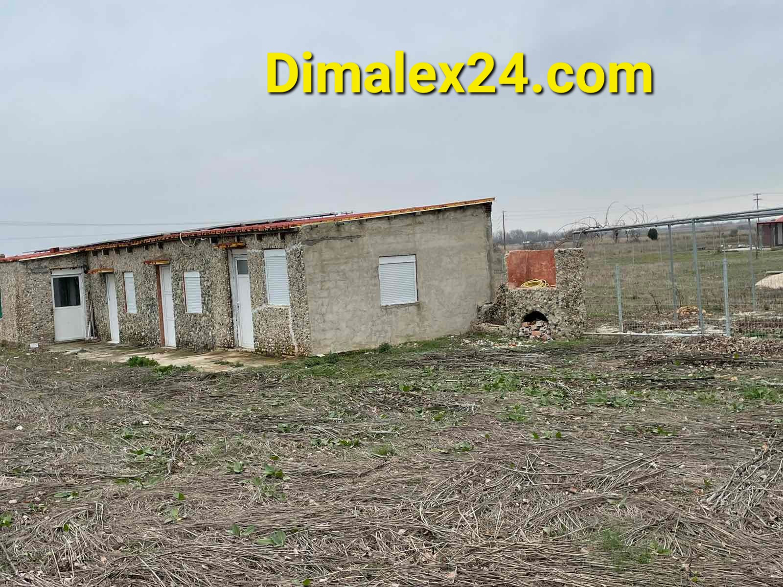 Exterior view of a modest house in rural area, surrounded by open land and a fence.