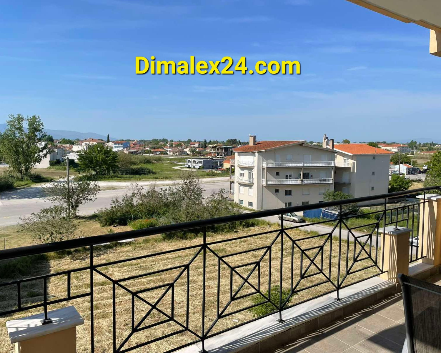 View from a balcony in Chrysoúpoli, Greece, showing surrounding houses and greenery.